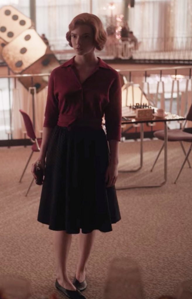 Beth Harmon, con blusa granate y falda negra